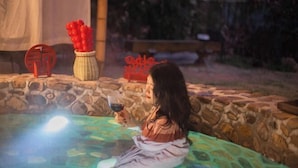 Une personne assise dans un bain à remous dont les parois sont en pierre, la nuit.
