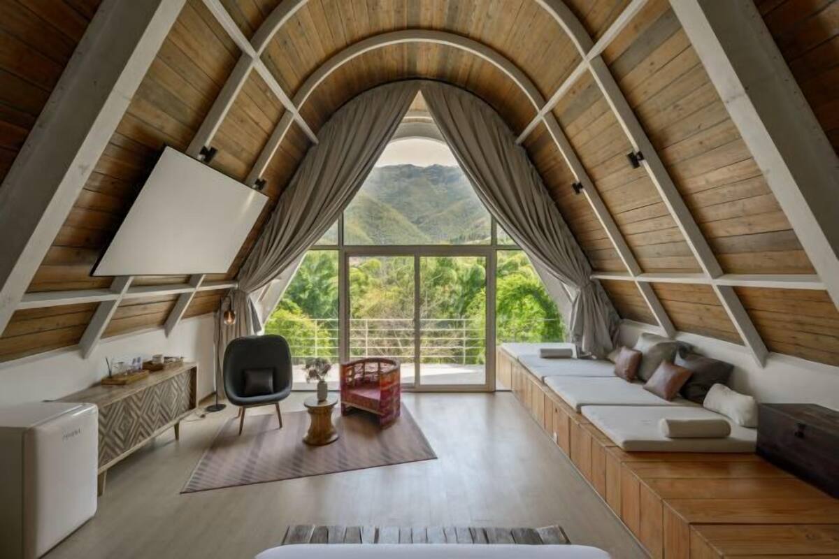 A cozy room with a sloped ceiling, a large window, a sofa, a chair, and a small table.