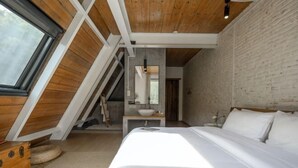 Une chambre avec un plafond en pente, un lit, une table de chevet, un miroir et une fenêtre.