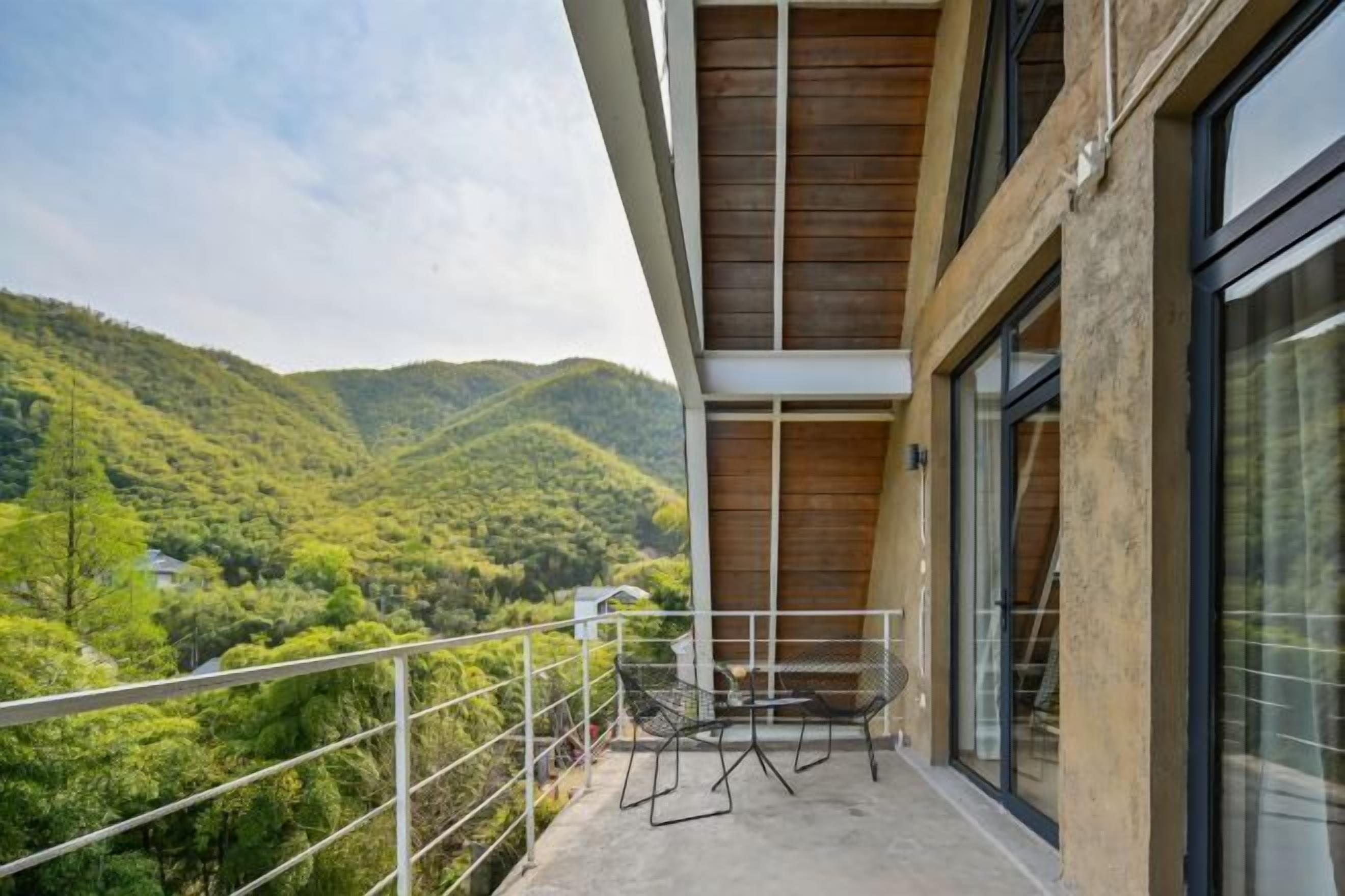 A balcony with a view of a green valley, a metal railing, and a glass door.