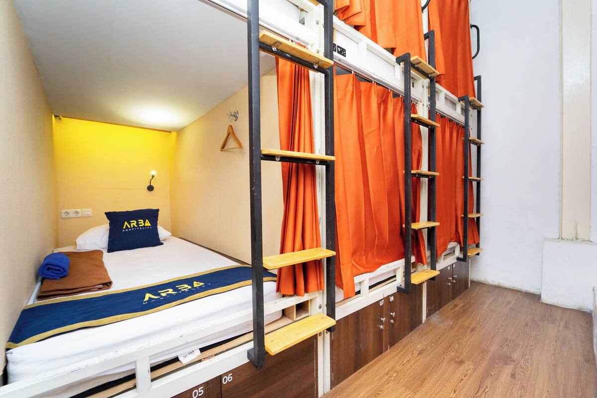 Een stapelbed met oranje gordijnen, een blauw kussen en een handdoek op het onderste bed.