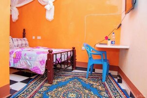 Una habitación pequeña y de colores brillantes con una cama, un sillón azul, una mesita y una alfombra estampada.
