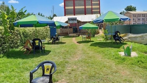 An outdoor seating area with tables and chairs under green umbrellas, a sign for 'Prestige Bar', and a tall building in the background. - Prestige Guest House Karatina (Karatina)