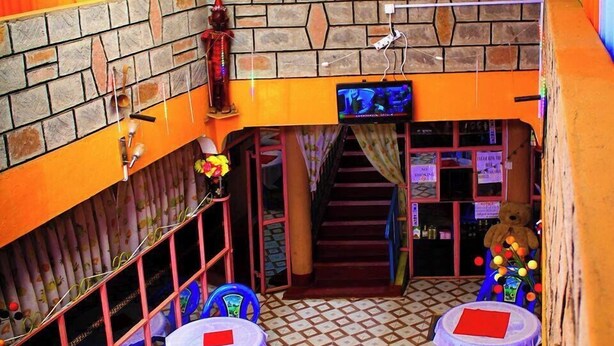 A restaurant with a stone wall, colorful curtains, two tables with chairs, and a staircase. - Prestige Guest House Karatina (Karatina)