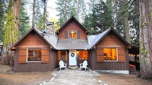Mökki, jossa on pääovi, kaksi sivusisäänkäyntiä ja kuisti, jossa on tuoleja.