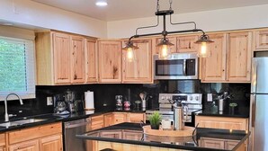 Une cuisine moderne avec des meubles en bois, un îlot central doté de tabourets, des appareils en acier inoxydable et un éclairage suspendu.
