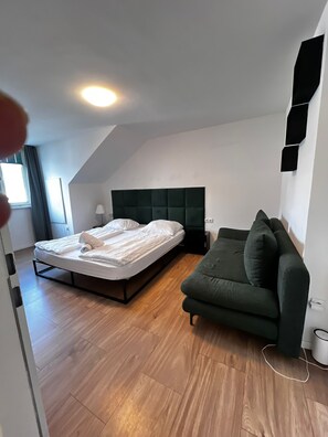 A modern bedroom with a bed, a green sofa, and a wooden floor. - Beautiful 2BR Apt Near U6 Schoepfwerk (Vienna)