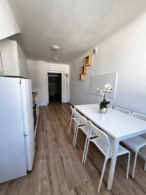 A modern kitchen with white appliances, a wooden floor, and a white dining table with chairs. - Beautiful 2BR Apt Near U6 Schoepfwerk (Vienna)