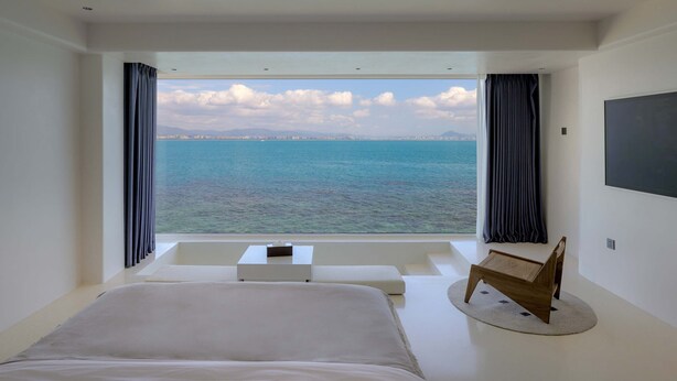 Une chambre avec un grand lit, une petite table, une chaise et une vue sur la mer.