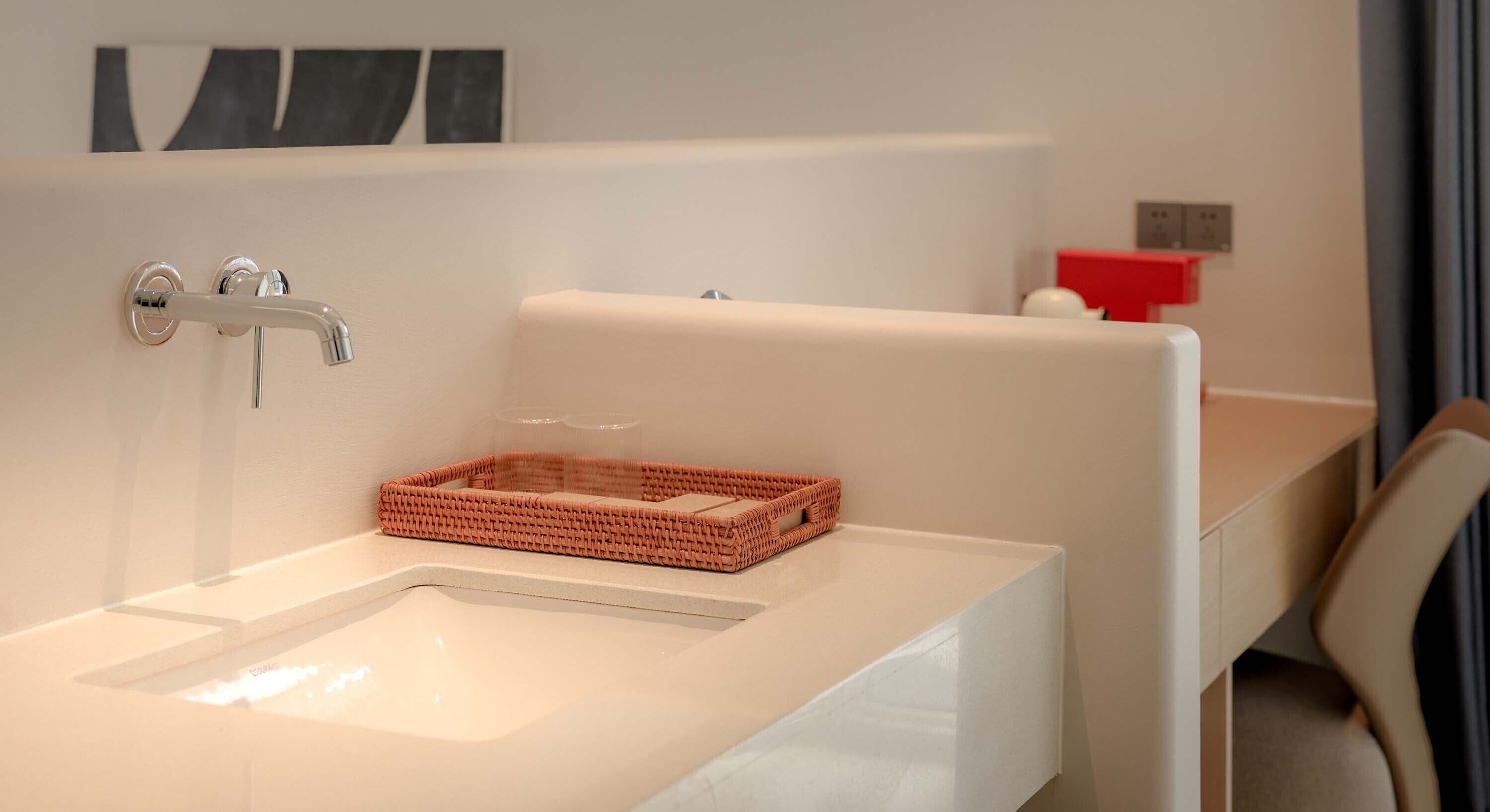 A modern bathroom with a white sink, a built-in bathtub, and a wicker basket on the sink.