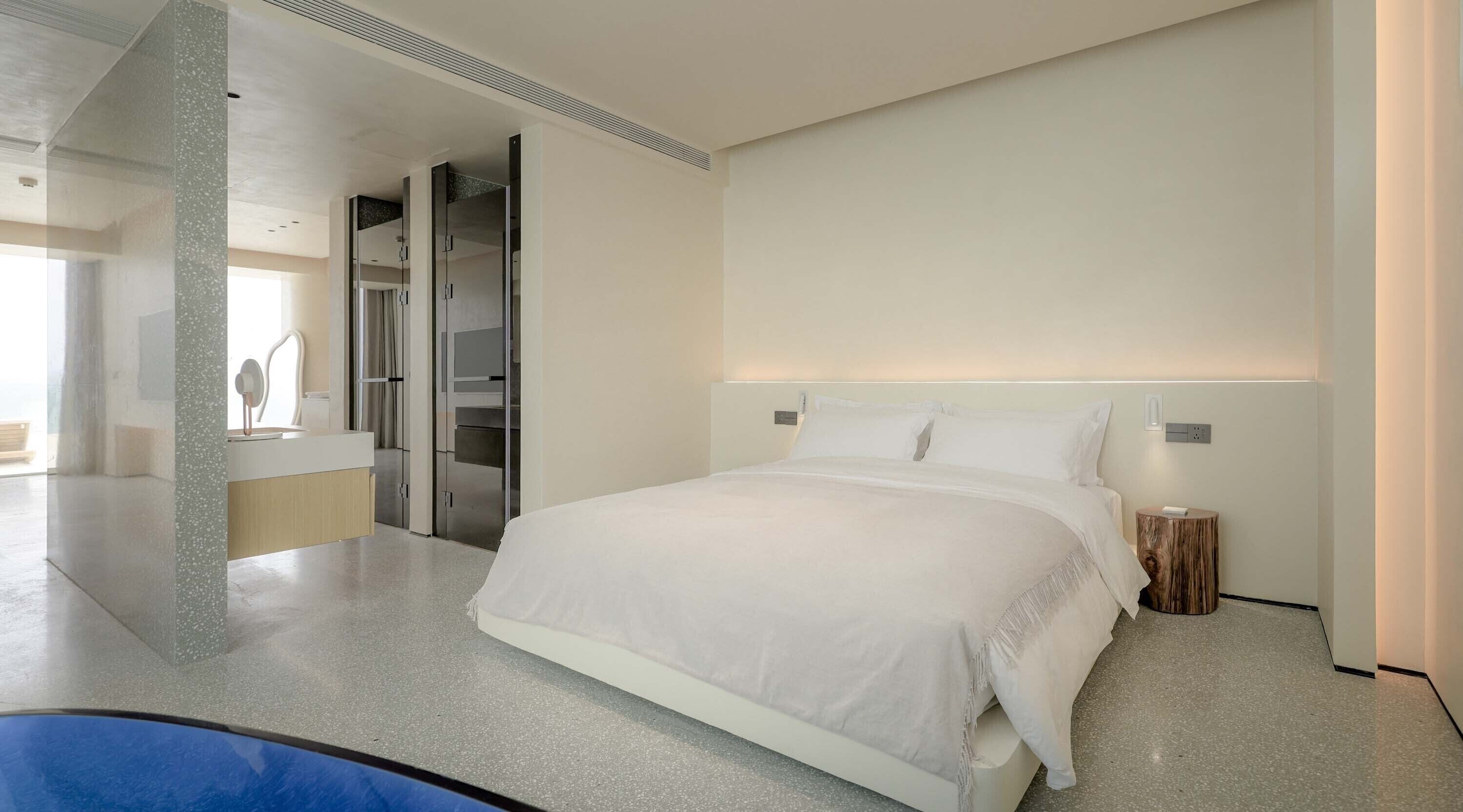 Una habitación de hotel moderna con una cama grande, un vestidor y un baño con ducha e inodoro.