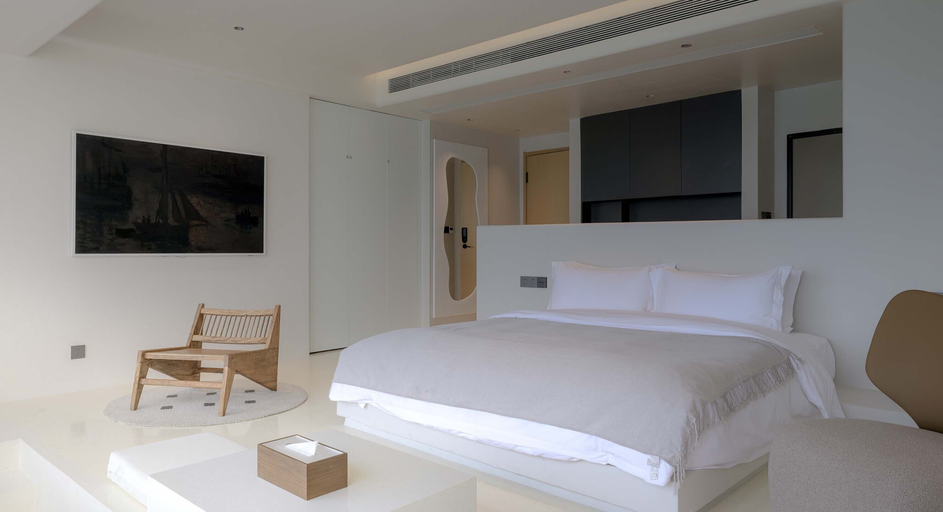 A modern bedroom with a large bed, a chair, a bedside table, and a painting on the wall.