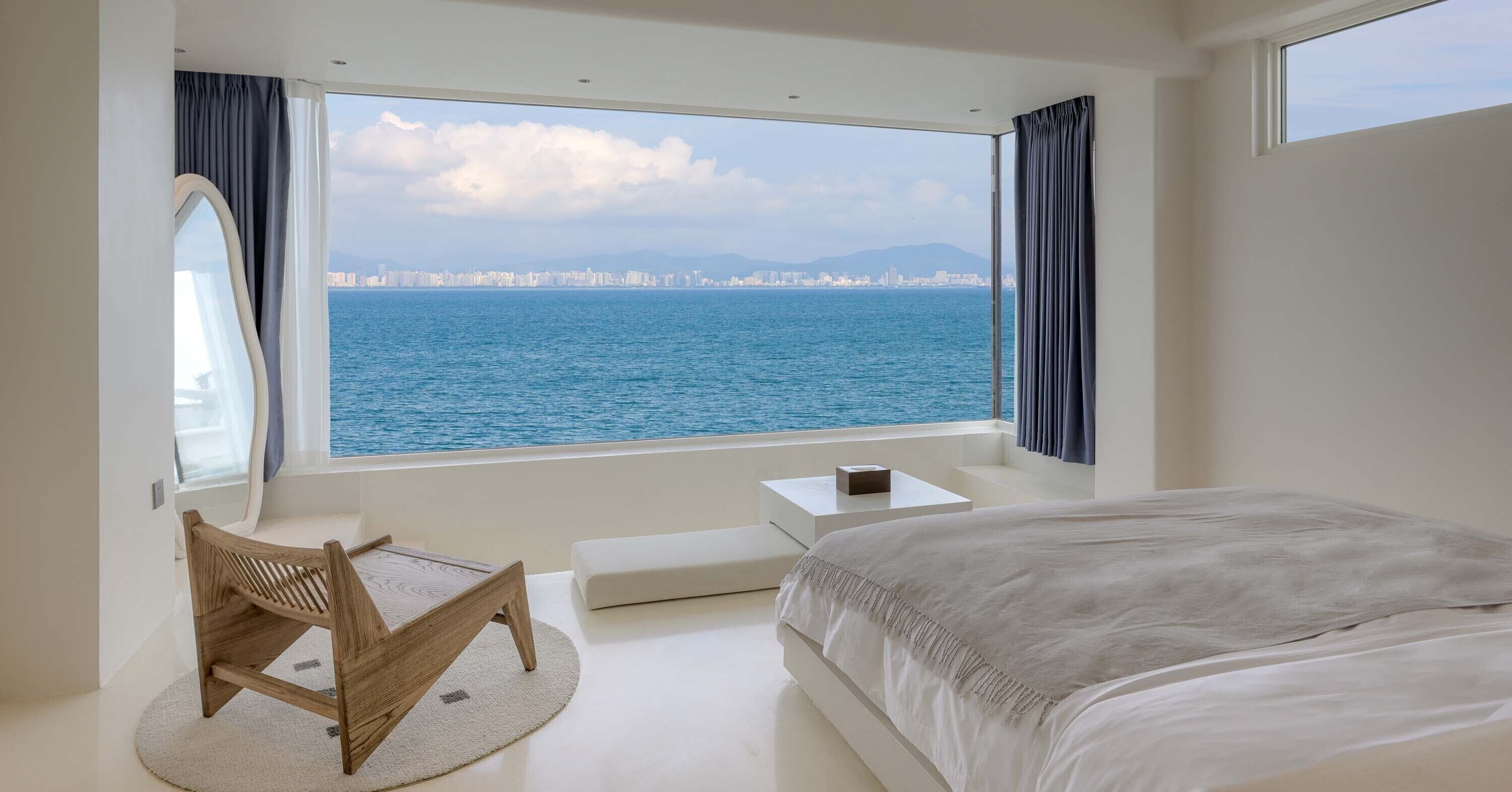 Un dormitorio con un gran ventanal que da a una masa de agua y un horizonte urbano distante.