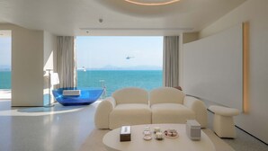 Une chambre d’hôtel moderne avec une grande fenêtre, une baignoire en verre bleu, un canapé et une table basse.