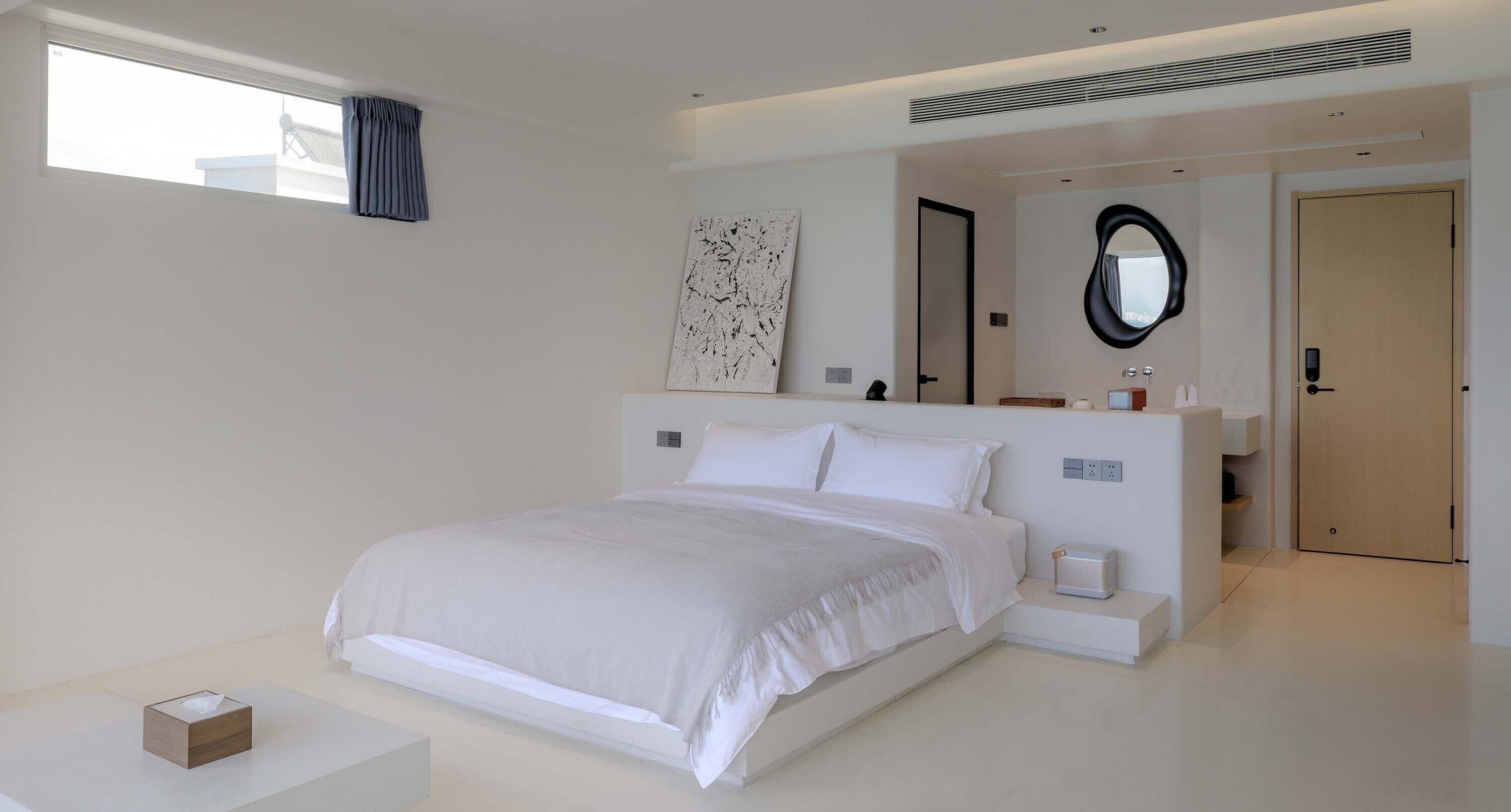 Une chambre moderne avec un grand lit, des tables de chevet, un miroir et une salle de bain visible à travers une porte ouverte.