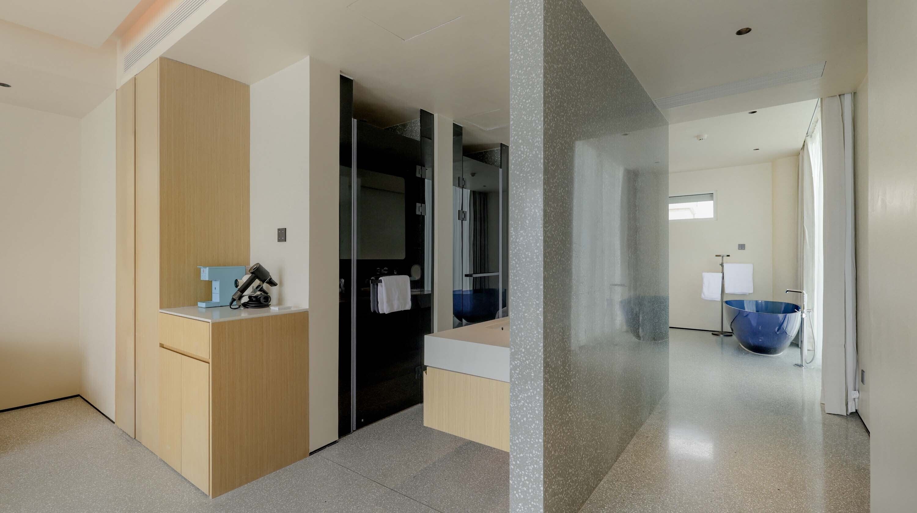 Ein moderner Hotelkorridor mit einem Holzerreptionsschalter, einem großen Spiegel und einem blauen Waschbecken im Badezimmer.