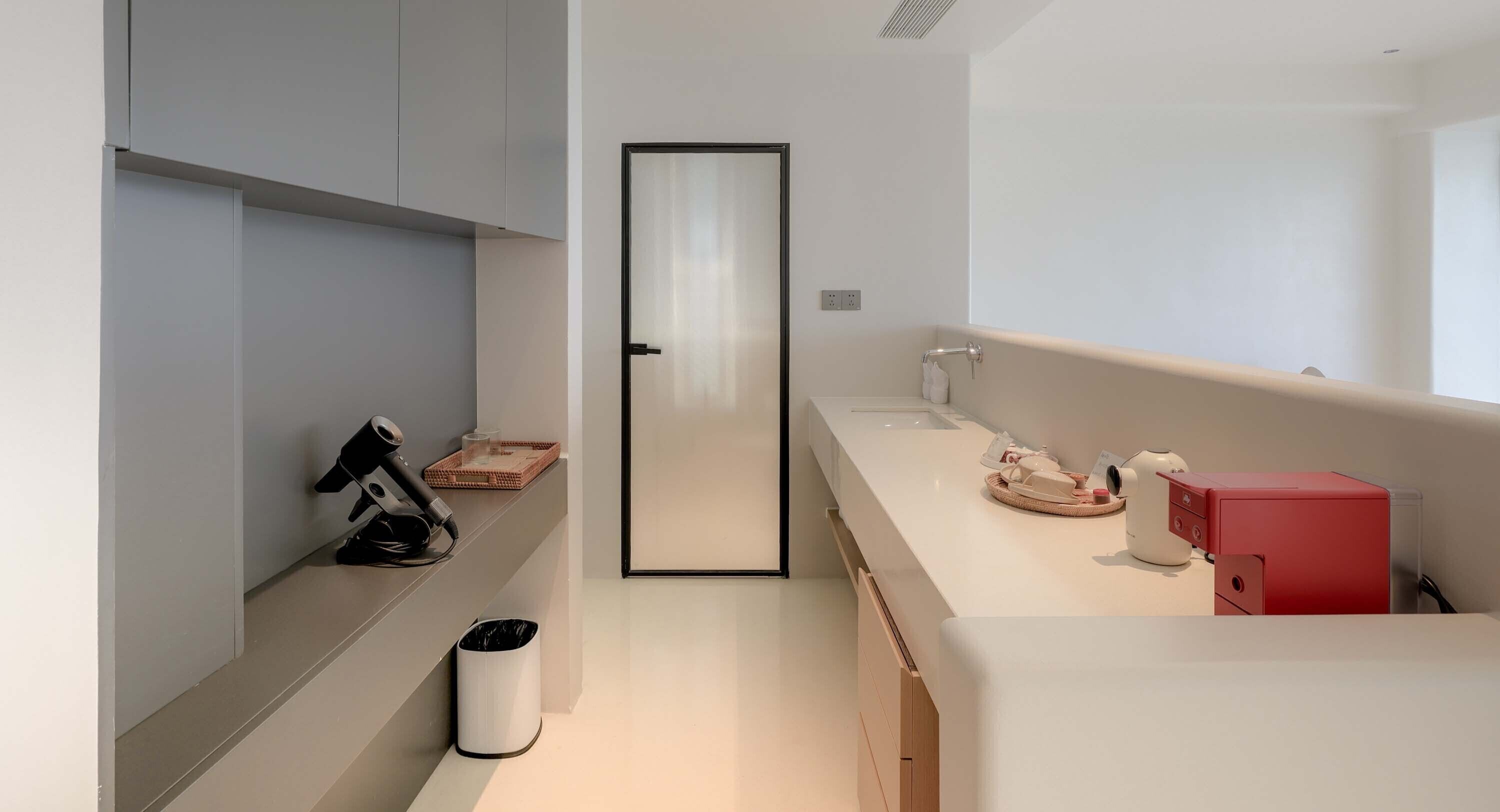 A modern kitchen with a white countertop, a red appliance, and a mirror.