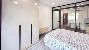 Una camera da letto con un letto, un armadio, una panca e una porta scorrevole in vetro che dà su un balcone.