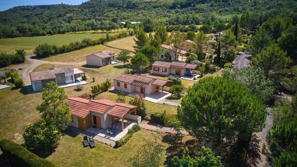 Quartiere residenziale con diverse case, alcune con tetti in tegole rosse, circondato dal verde e colline sullo sfondo.