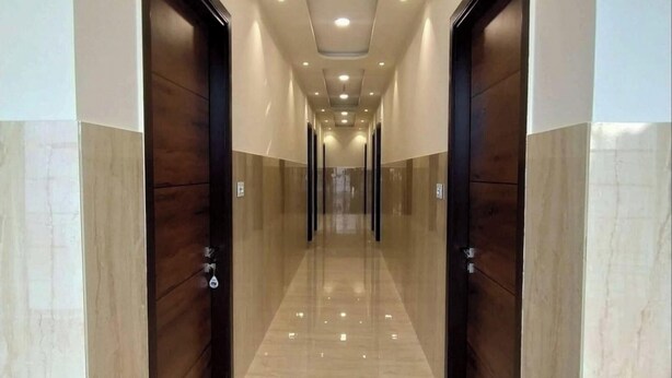 A long, well-lit hallway with marble flooring and wooden doors on either side. - MI Rooms (Hoshiarpur)