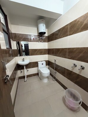 A bathroom with a toilet, sink, and shower. There is a water heater mounted on the wall. - Hotel star Residency (Gurugram)