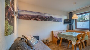 Una sala de estar acogedora con un sofá, una mesa de comedor con sillas y un cuadro grande de un paisaje montañoso en la pared.