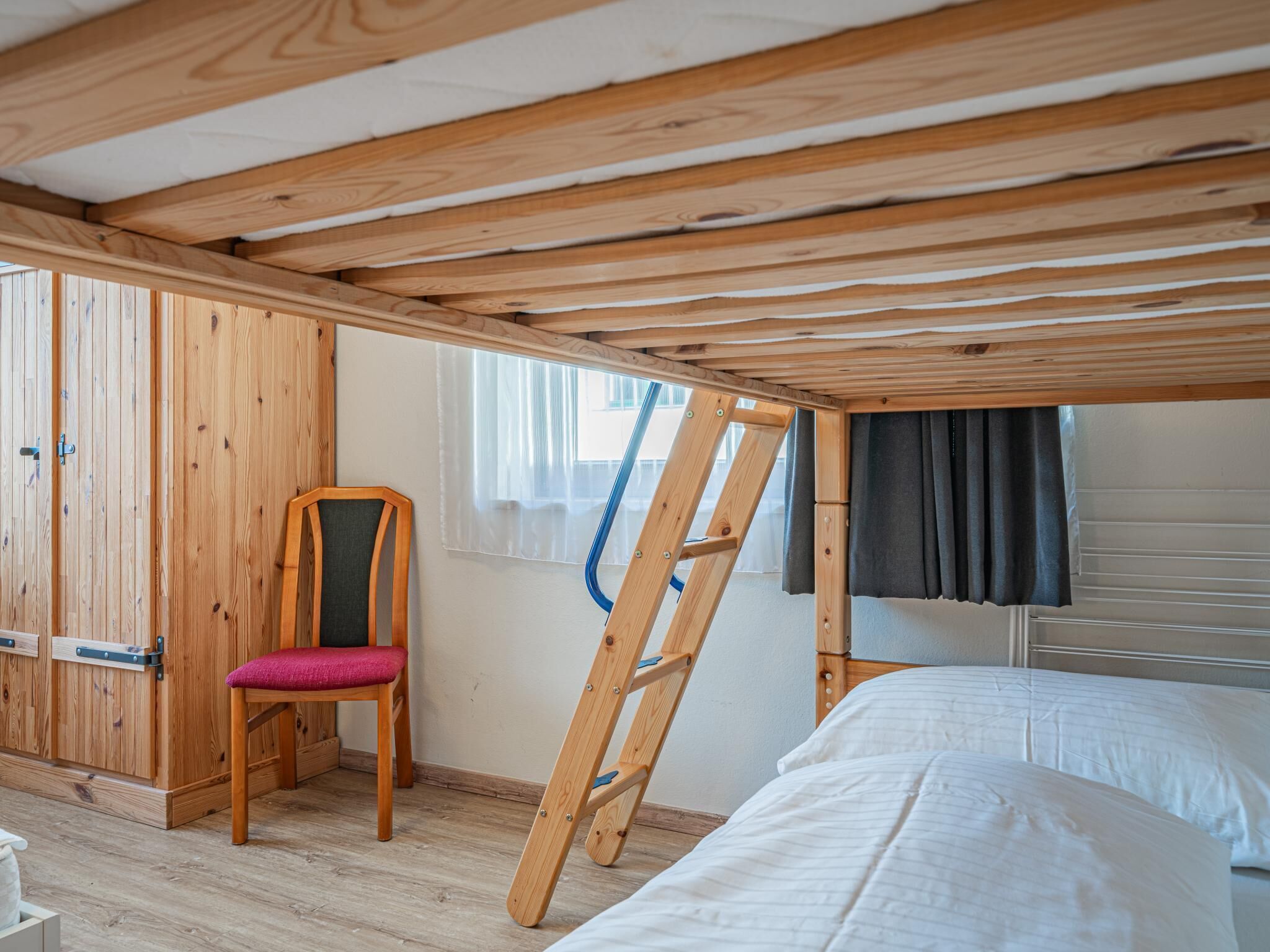 A wooden cabin with a loft bed, a chair, and a ladder.