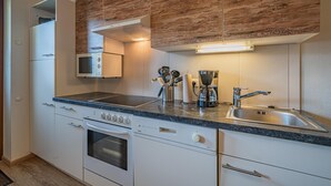 Una cocina moderna con armarios blancos, horno empotrado, microondas, cafetera y un lavamanos de acero inoxidable.