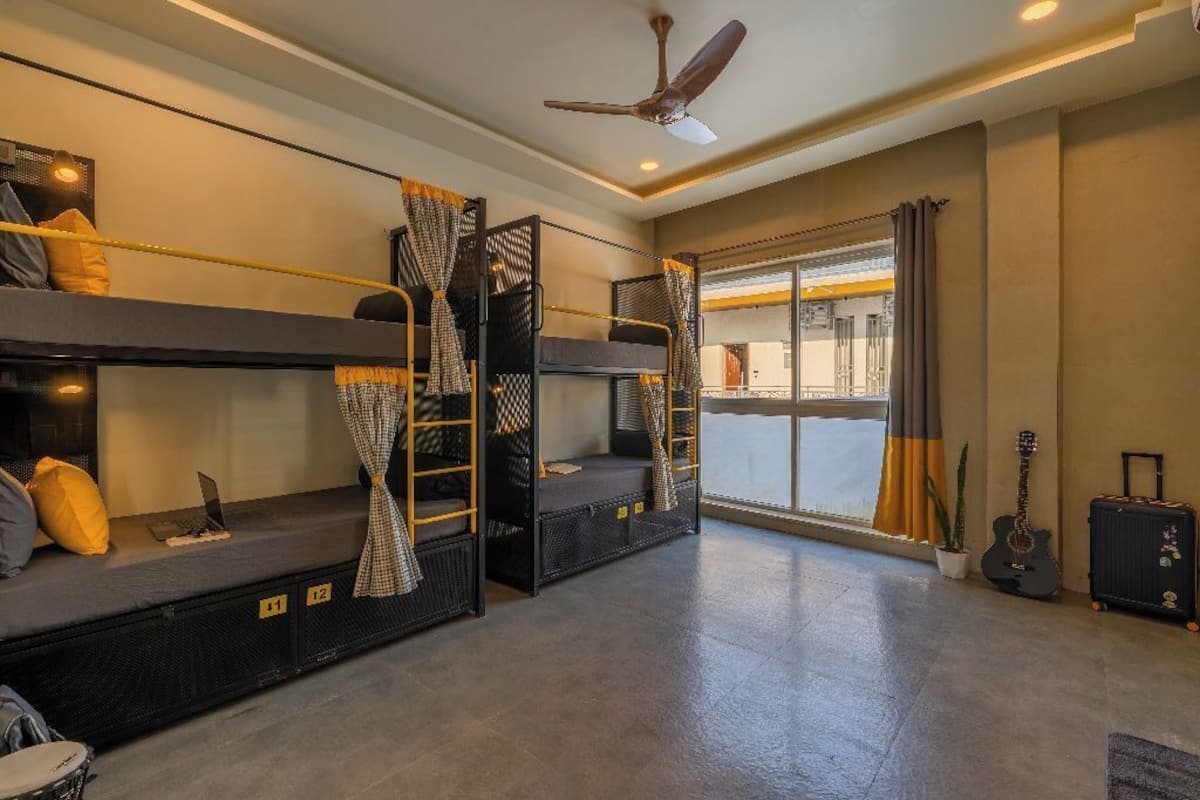 A room with bunk beds, a ceiling fan, a guitar, and a suitcase.