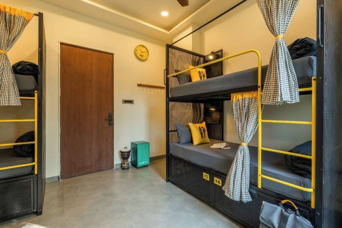 A dormitory room with bunk beds, a wooden door, a clock, and a small trash bin.
