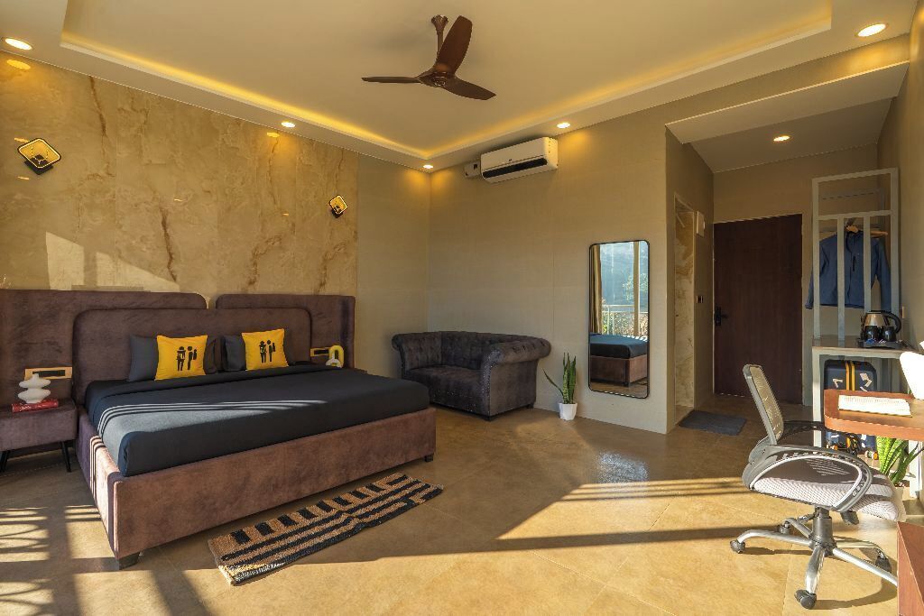 A modern bedroom with a large bed, a desk, and a view of the outdoors.