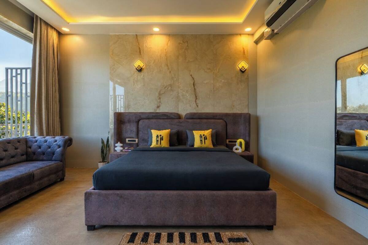 A bedroom with a large bed, a sofa, a nightstand, and a mirror.