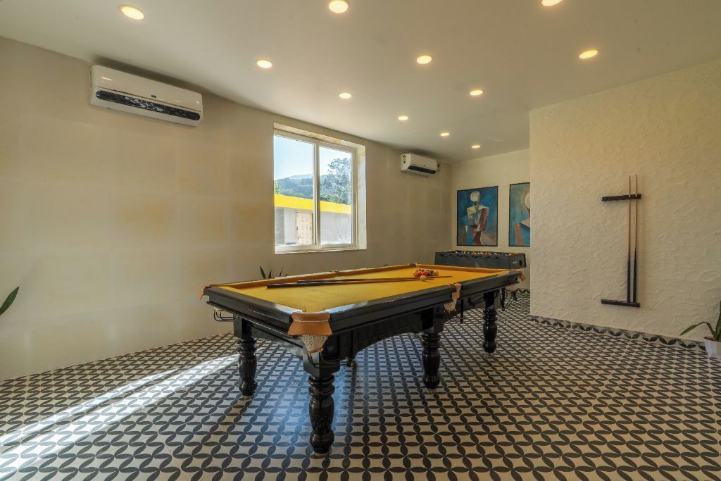 A pool table in a room with patterned flooring, a window, and an air conditioning unit on the wall.