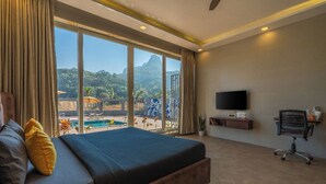 A hotel room with a large bed, a TV, and a view of a pool and mountains. - The Hosteller Bam Lonavala, Tiger Point (Paud)