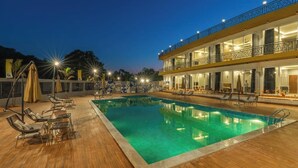 A pool area with lounge chairs and umbrellas, a building with balconies, and a clear night sky. - The Hosteller Bam Lonavala, Tiger Point (Paud)
