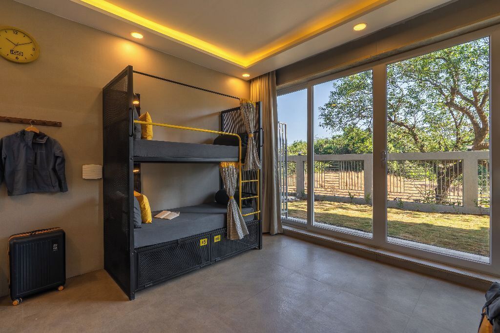 A bunk bed room with a large window, a clock, and a suitcase.