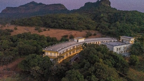 A large, modern building with a curved roof, surrounded by dense forest and hills. - The Hosteller Bam Lonavala, Tiger Point (Paud)
