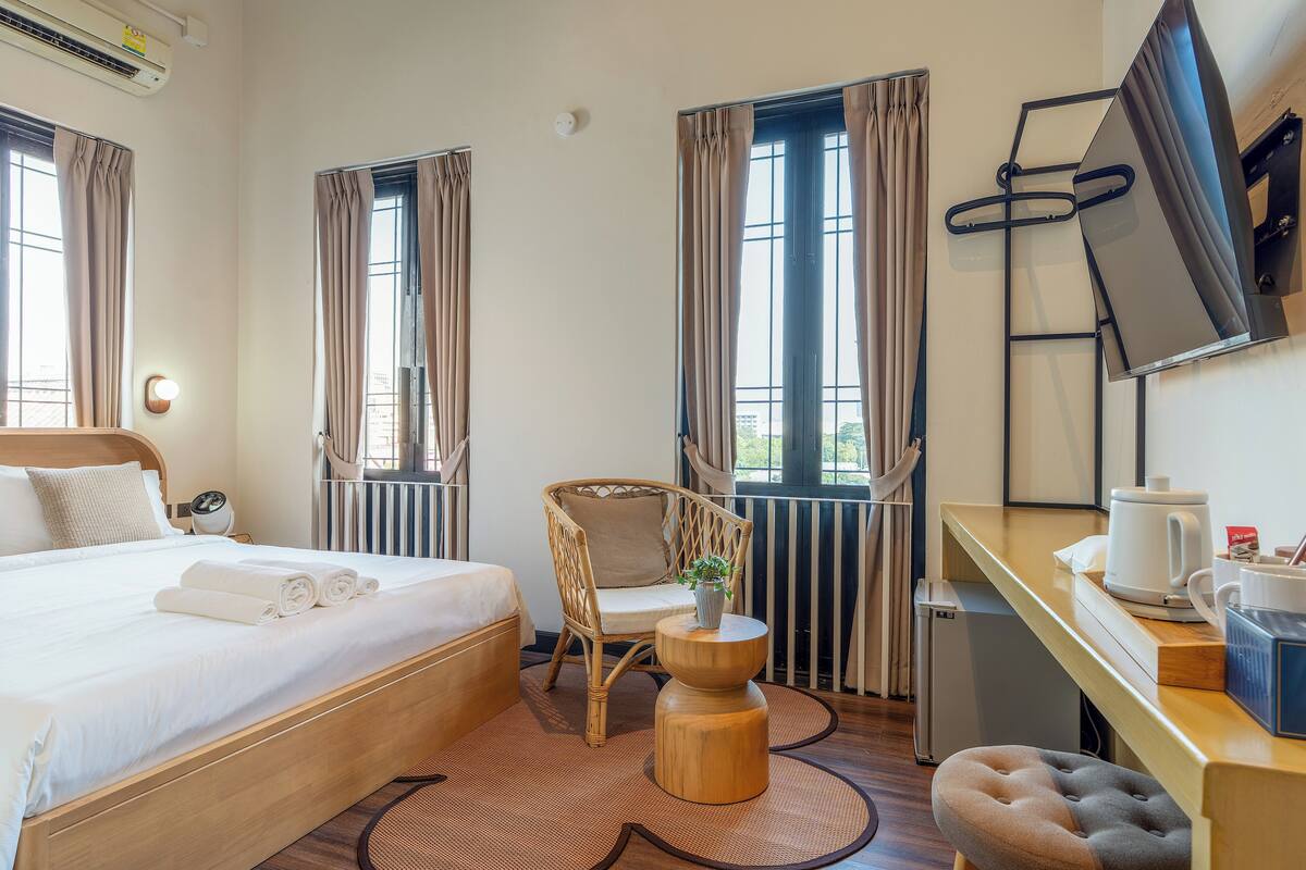 A hotel room with a bed, a chair, a desk, a TV, and a radiator.