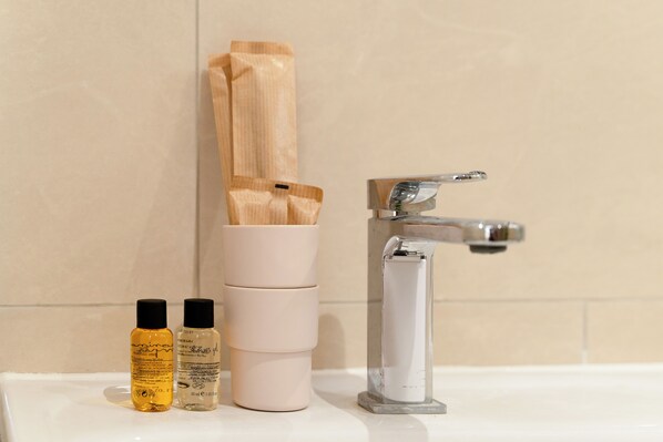 Une salle de bain avec un lavabo blanc, deux bouteilles de liquide, un distributeur de serviettes en bois et un robinet chromé.