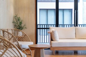 Une pièce comprenant un canapé, des fauteuils, une petite table et une grande fenêtre donnant sur un immeuble.