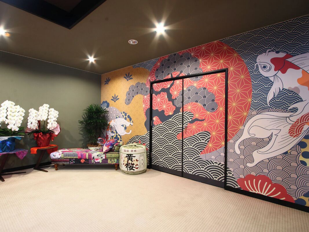 A traditional Japanese room with tatami flooring, a low table with a cushion, a low wooden cabinet, and a large wall painting.