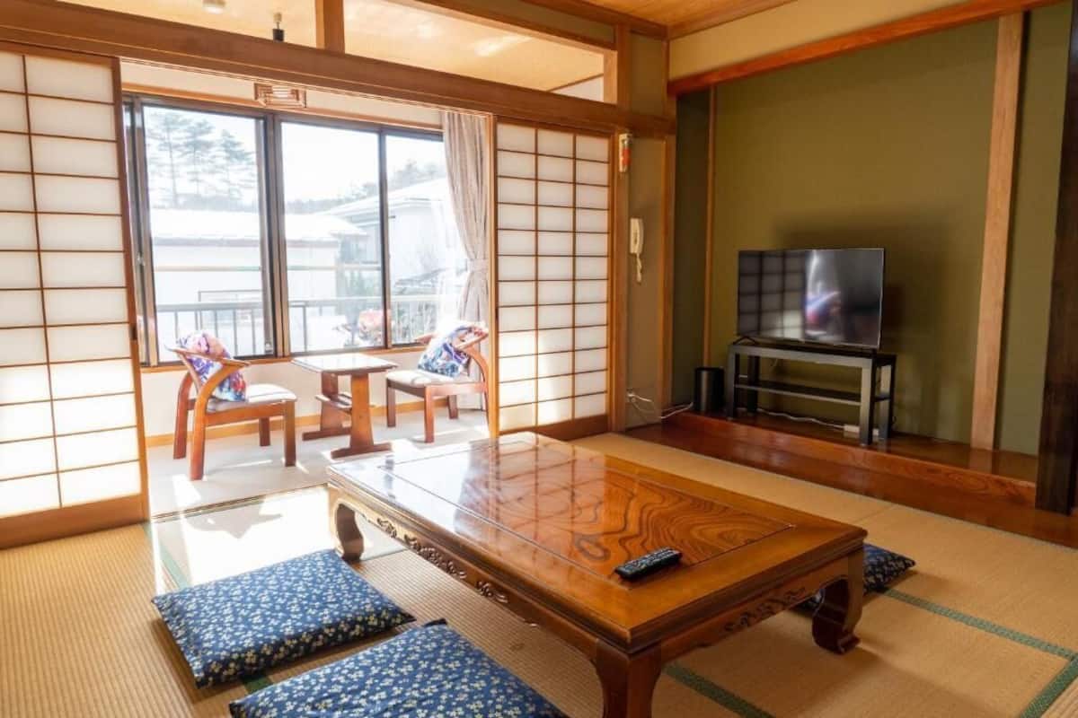 Ein traditioneller japanischer Raum mit Tatami-Boden, einem niedrigen Holztisch und einem Fernseher auf einem Podest.