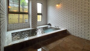 A spa room with a large bathtub, tiled walls, and a window. - Kujiranoonaka (Yamanakako)