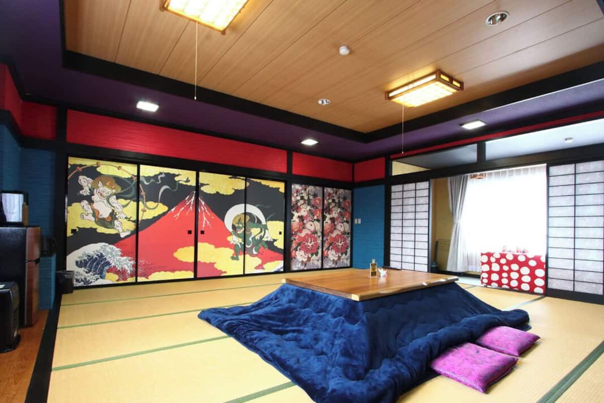 Ein Raum mit Tatami-Matten, einem niedrigen Holztisch, Kissen und traditionellen japanischen Kunstwerken an den Wänden.