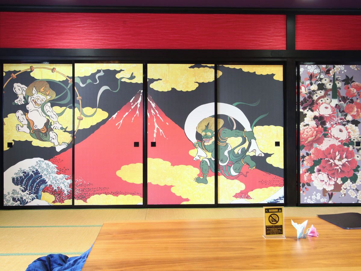Ein Zimmer mit traditioneller japanischer Schiebetür, verziert mit Kunstwerken, einem Holztisch und einem Warnschild.