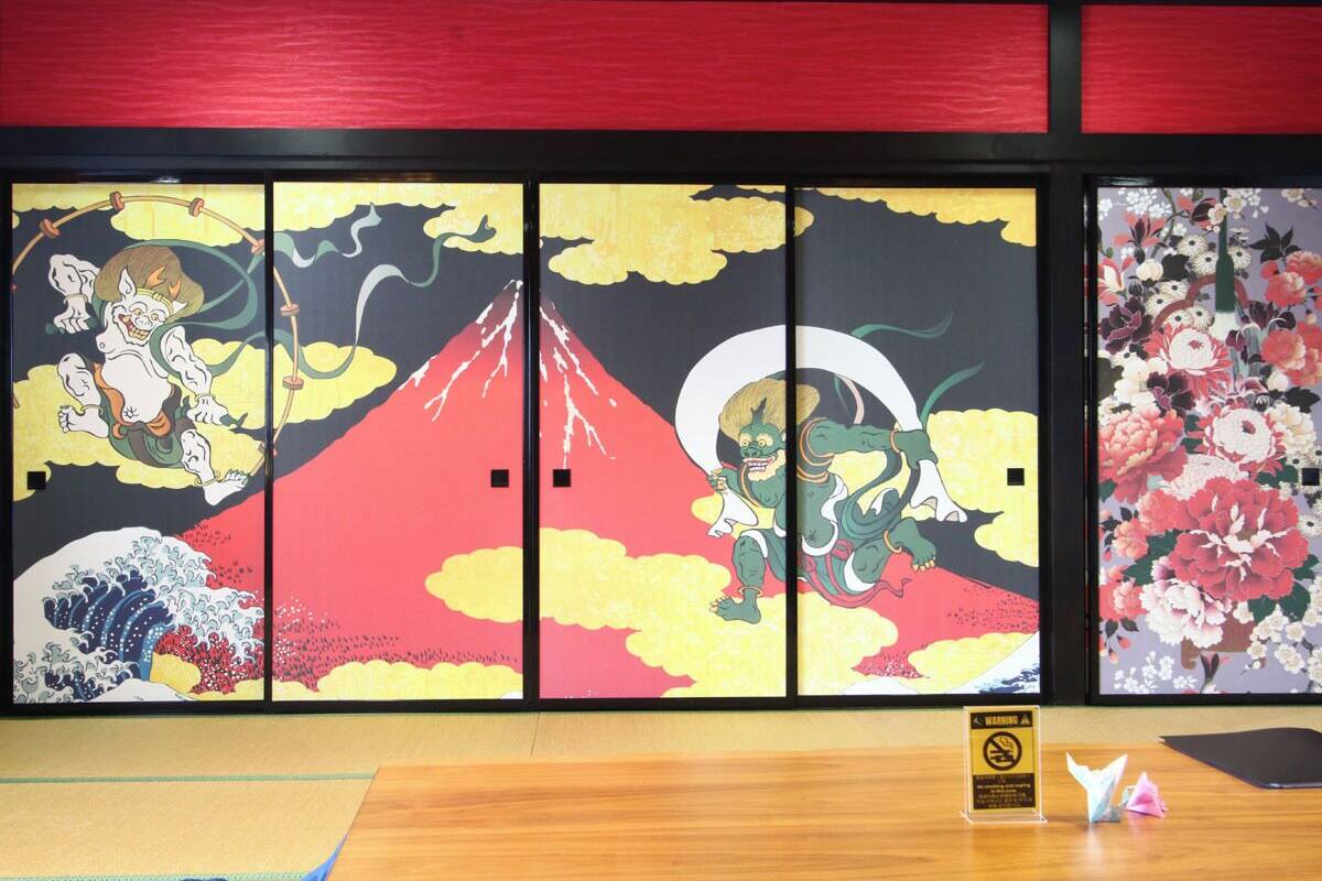 Ein Zimmer mit traditioneller japanischer Schiebetür, verziert mit Kunstwerken, einem Holztisch und einem Warnschild.