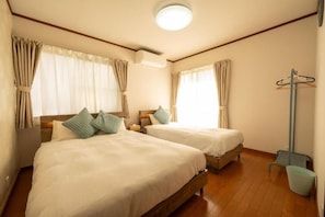 Ein Hotelzimmer mit zwei Einzelbetten, Holzboden, Deckenventilator und einem Fenster mit Vorhängen.