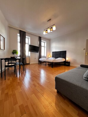 A modern hotel room with a bed, a desk with a chair, a TV mounted on the wall, and a window with curtains. - Pleasant 2BR Apt Near U6 Schöpfwerk (Vienna)