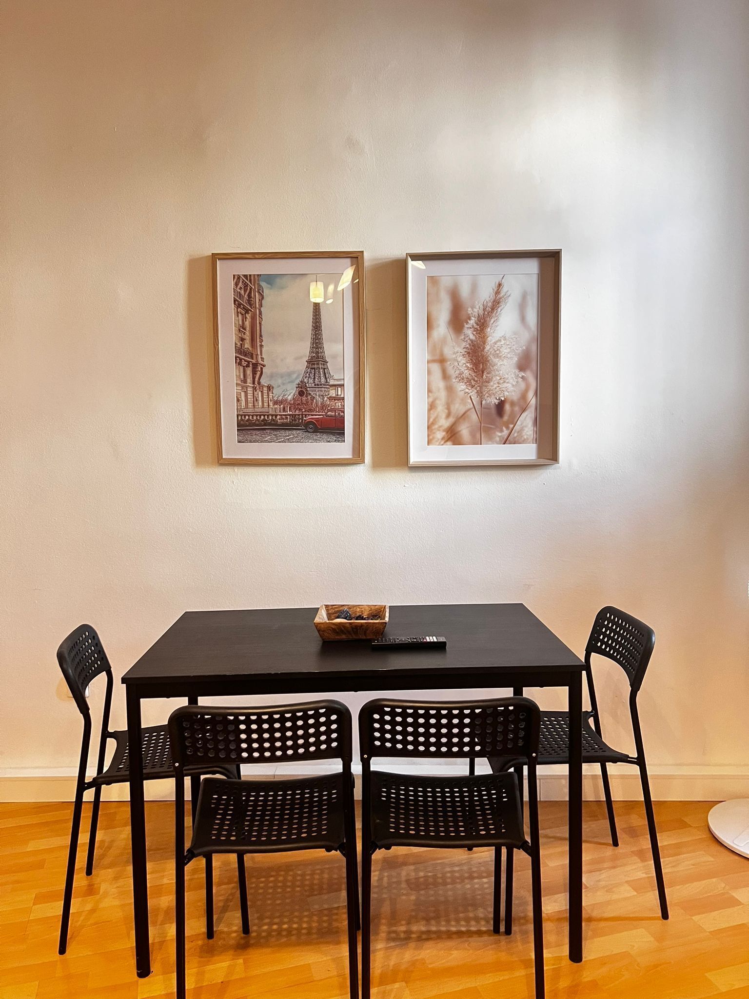 A dining area with a black table and four black chairs. Two framed pictures are hung on the wall above the table.