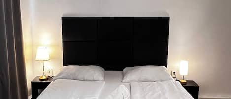 A neatly made bed with white linens, two bedside tables with lamps, and a dark headboard.